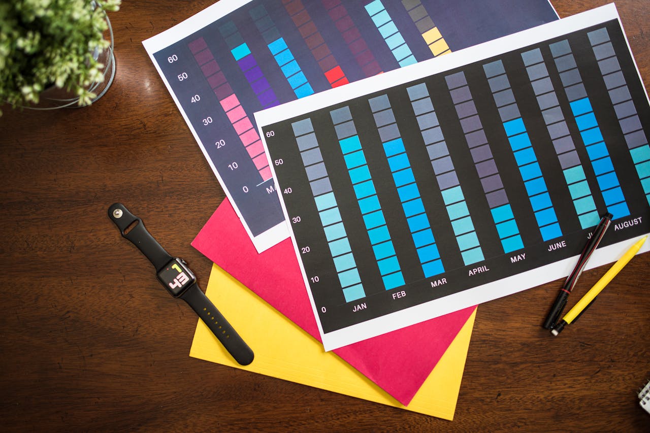 Flat lay of colorful business charts with a smartwatch, pens, and documents on a table.